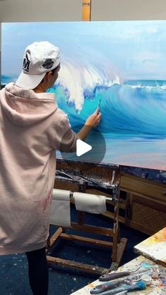 a woman is painting an ocean wave on the easel