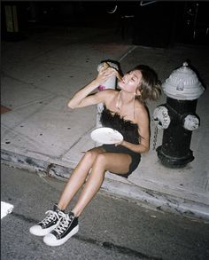 a woman sitting on the curb drinking from a bottle