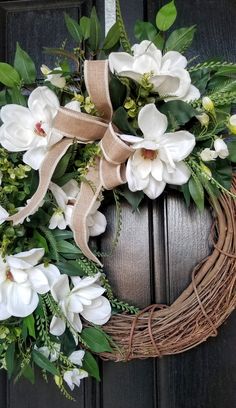 a wreath with white flowers and greenery hanging on a door