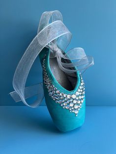 a pair of blue ballet shoes with white ribbon and jeweled shoelaces, on a blue background