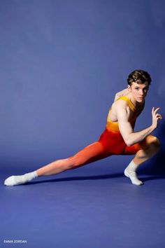 a young man in red and yellow leotard posing for a photo on a blue background