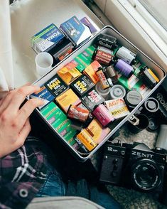 a person sitting on the floor with an open suitcase filled with various types of items