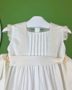 A gorgeous off-white dress for special occasions, made with a lightweight linen fabric and laces. It has buttons on the back for closure and satin strings to form two bows on the sides. Dry clean Made in Spain Final Sale, no exchanges nor returns are accepted White Formal Dress With Tie Back, Summer Baptism Dress With Bow, White Sleeveless Dress With Ribbon, Elegant Summer Baptism Dress For Garden Party, Elegant Cream Baptism Dress For Summer, White Sleeveless Dress For Ceremony, Elegant Cream Dress With Bow, White Wedding Dress With Ribbon Detail, White Spring Dress With Satin Bow