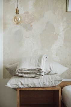 pillows and blankets stacked on top of each other in front of a wall with a light fixture