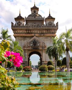 the entrance to an ornately designed park with water and flowers in front of it