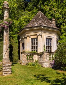 an old stone building sitting in the middle of a lush green field next to trees