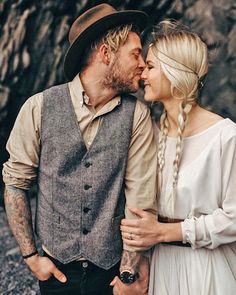 a man and woman standing next to each other in front of a rock wall holding hands