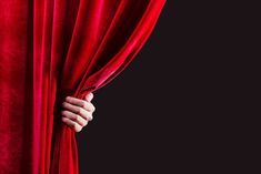 a hand is opening the curtain to reveal red velvet fabric on a black background with space for text