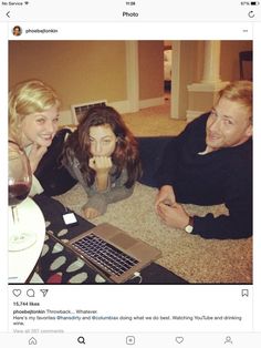 two women and a man sitting on the floor in front of a laptop