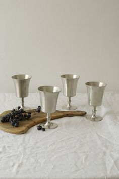 four silver cups on a wooden board with grapes