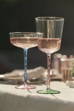 two wine glasses sitting next to each other on top of a white cloth covered table