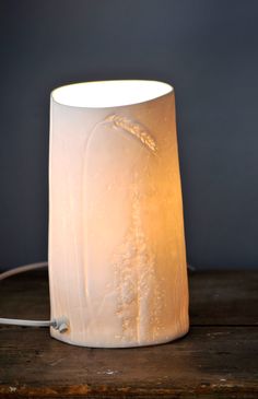 a white lamp sitting on top of a wooden table next to a black wall and floor