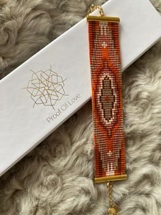 an orange and white beaded bracelet with a gold chain hanging from it's end