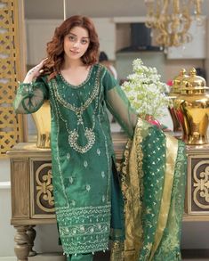 a woman standing in front of a mirror wearing a green dress and gold jewelry necklace