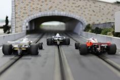 three toy race cars on a track under a bridge