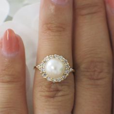 a close up of a person's hand with a pearl and diamond ring on it