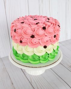 a cake with pink, green and white frosting on a plate sitting on a wooden table