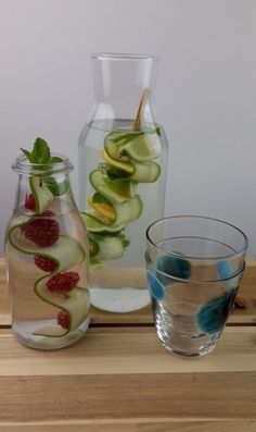 two vases filled with cucumber and raspberries next to each other