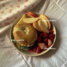 a bagel sandwich, sliced apples and strawberries on a plate with the words written below it