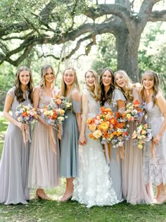 a group of women standing next to each other in front of a tree with orange and yellow flowers