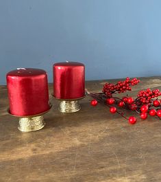 two red candles sitting on top of a wooden table next to some berries and twigs