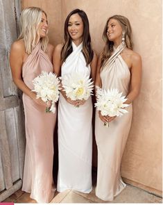 three beautiful women standing next to each other holding white flowers and bouquets in their hands