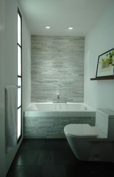 a white toilet sitting next to a bath tub in a bathroom under a light fixture