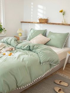 a bed with green comforter and pillows in a white room next to a window