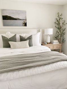 a bed with white linens and pillows in a bedroom next to a painting on the wall