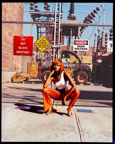 a woman in orange pants is squatting on the sidewalk next to a construction site