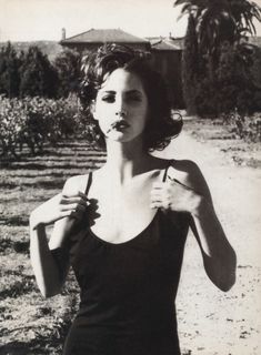 black and white photograph of a woman brushing her teeth in front of a dirt road