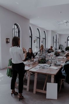 a group of people sitting around a wooden table in a large room with windows on both sides