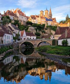 an old bridge over a small river with buildings on the hill in the back ground