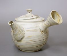 a white ceramic teapot with a lid on it's side, sitting against a gray background