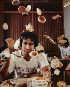 a man sitting at a table with food flying from his head and hands in the air