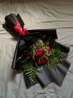 a bouquet of red roses and ferns wrapped in black paper on top of a bed