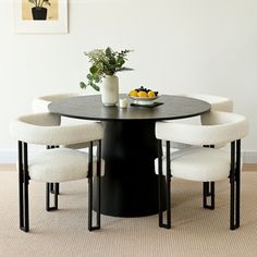 a black table with four white chairs and a bowl of oranges on the top