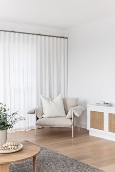 a living room with a couch, coffee table and white curtained window behind it