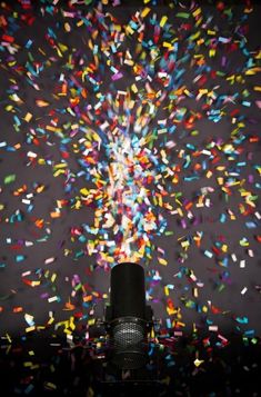 a microphone with colorful confetti in the air and a black background that is filled with multicolored sprinkles