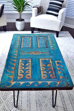 a coffee table that has been painted with blue and gold designs on it, sitting in front of a white chair