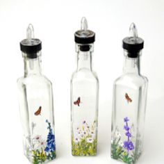 three glass bottles with flowers and butterflies painted on the sides, one is empty while the other is closed