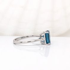 This beautiful ring features a 2.38-carat emerald cut London topaz with two earth-mined baguette diamond accents, all set in solid 14K gold. The ring exudes both elegance and durability, making it suitable for everyday wear or special occasions! This ring is made with solid 14K Gold and naturally Earth mined SI / G-H diamonds. As listed, this ring is ready to ship. If you're interested in purchasing this setting with a different center stone please message us! Emerald-cut Topaz Ring In 14k White Gold, Emerald Cut Topaz Ring In 14k White Gold, Modern Emerald Cut Topaz Ring, Emerald-cut Sapphire Ring With Topaz Accent Stones, Blue Topaz Baguette Cut Ring, Baguette Cut Blue Topaz Ring, London Topaz, Designer Silver Jewellery, London Blue Topaz Ring