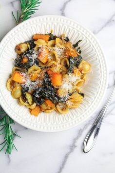 a white plate topped with pasta and vegetables covered in parmesan cheese on top of a marble counter