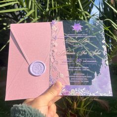 a person holding up a pink and purple wedding card with a wax stamp on it