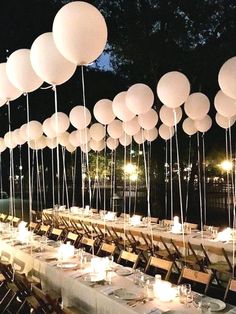 a long table with many white balloons hanging from it's poles and place settings