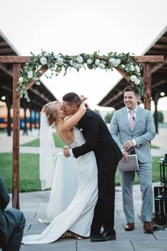 a bride and groom kissing in front of their wedding party at the end of an outdoor ceremony