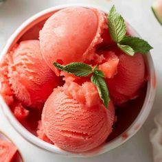 three scoops of watermelon ice cream in a bowl with mint leaves on top