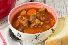 a white plate topped with a bowl of soup next to a slice of bread