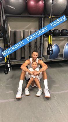 a man holding a baby while sitting on top of a gym floor