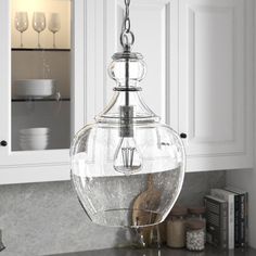 a glass bowl hanging from the ceiling in a kitchen with white cabinets and marble counter tops